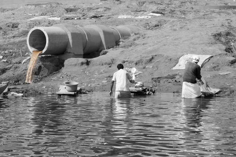 Wastewater Reuse: Washermen doing laundry at the confluence of raw sewage and river water on the banks of river Ganga in Varanasi, Uttar Pradesh